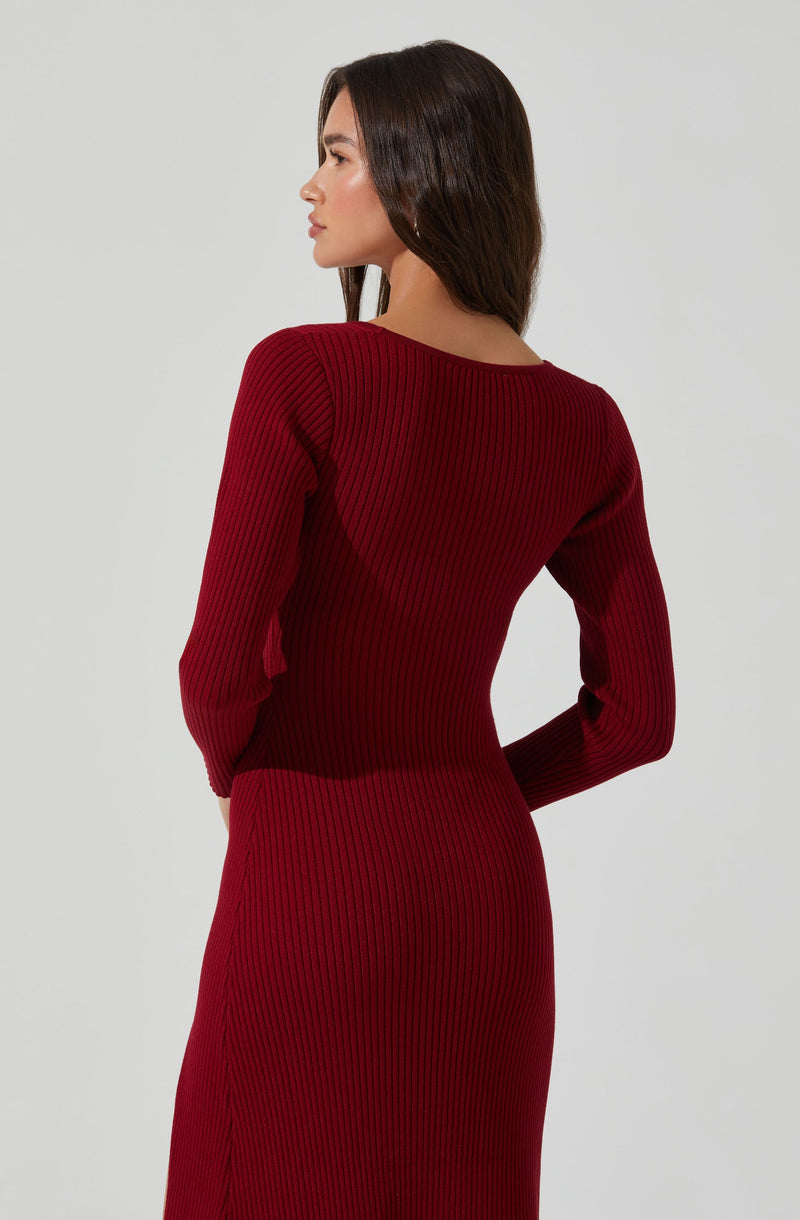 A woman is wearing a fitted, long-sleeved, ribbed dress in a deep red color. The dress has a round neckline and features vertical ribbing throughout.