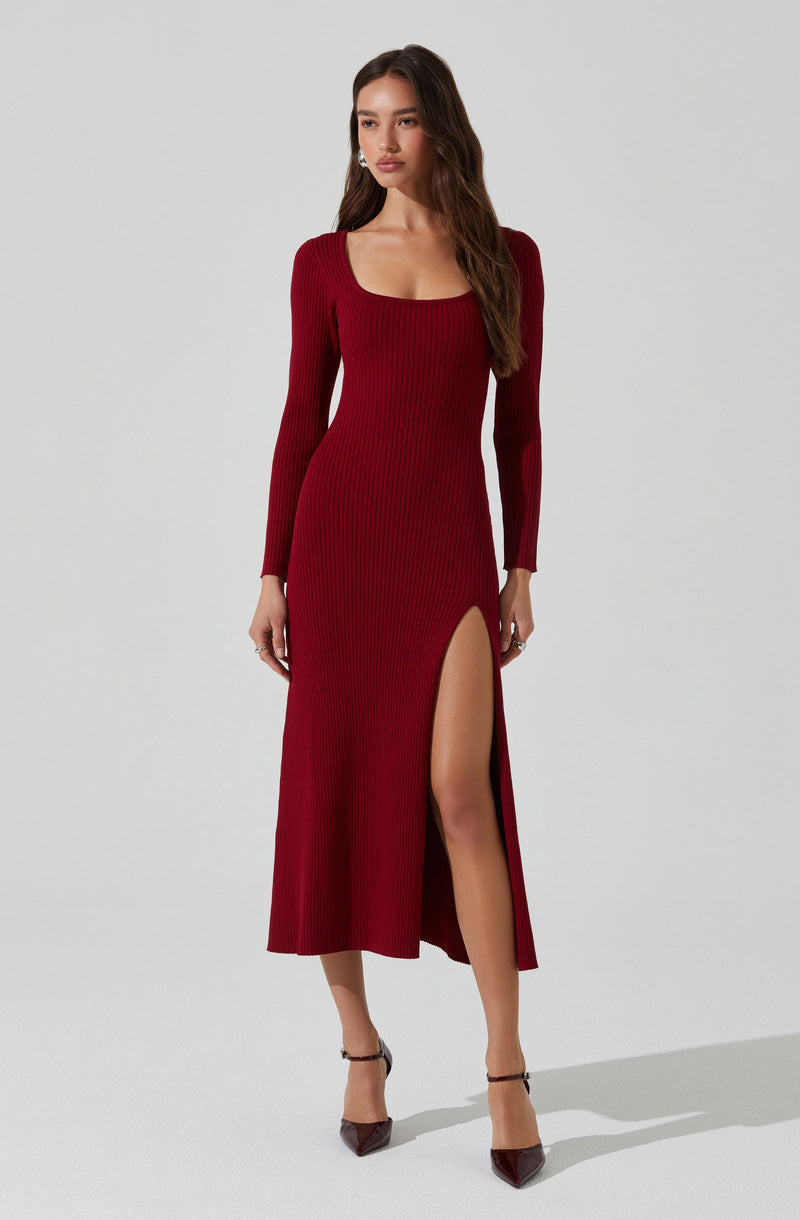 A woman is wearing a long, fitted, ribbed knit dress in a deep red color. The dress features long sleeves, a square neckline, and a high slit on the left side, revealing her leg. She is wearing dark-colored high-heeled shoes with ankle straps.