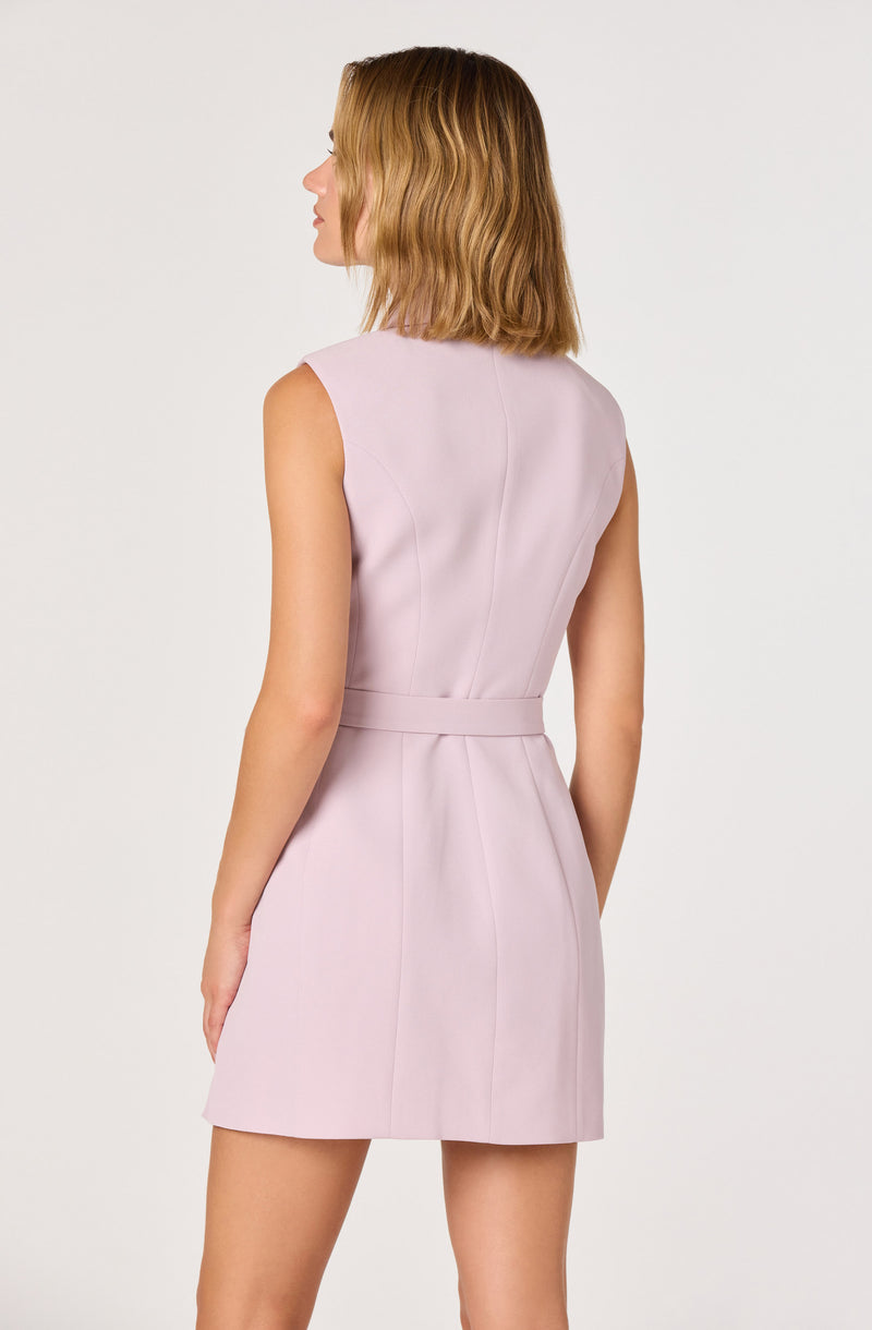Woman in pastel pink sleeveless dress with a fitted waist and short hemline, standing sideways.