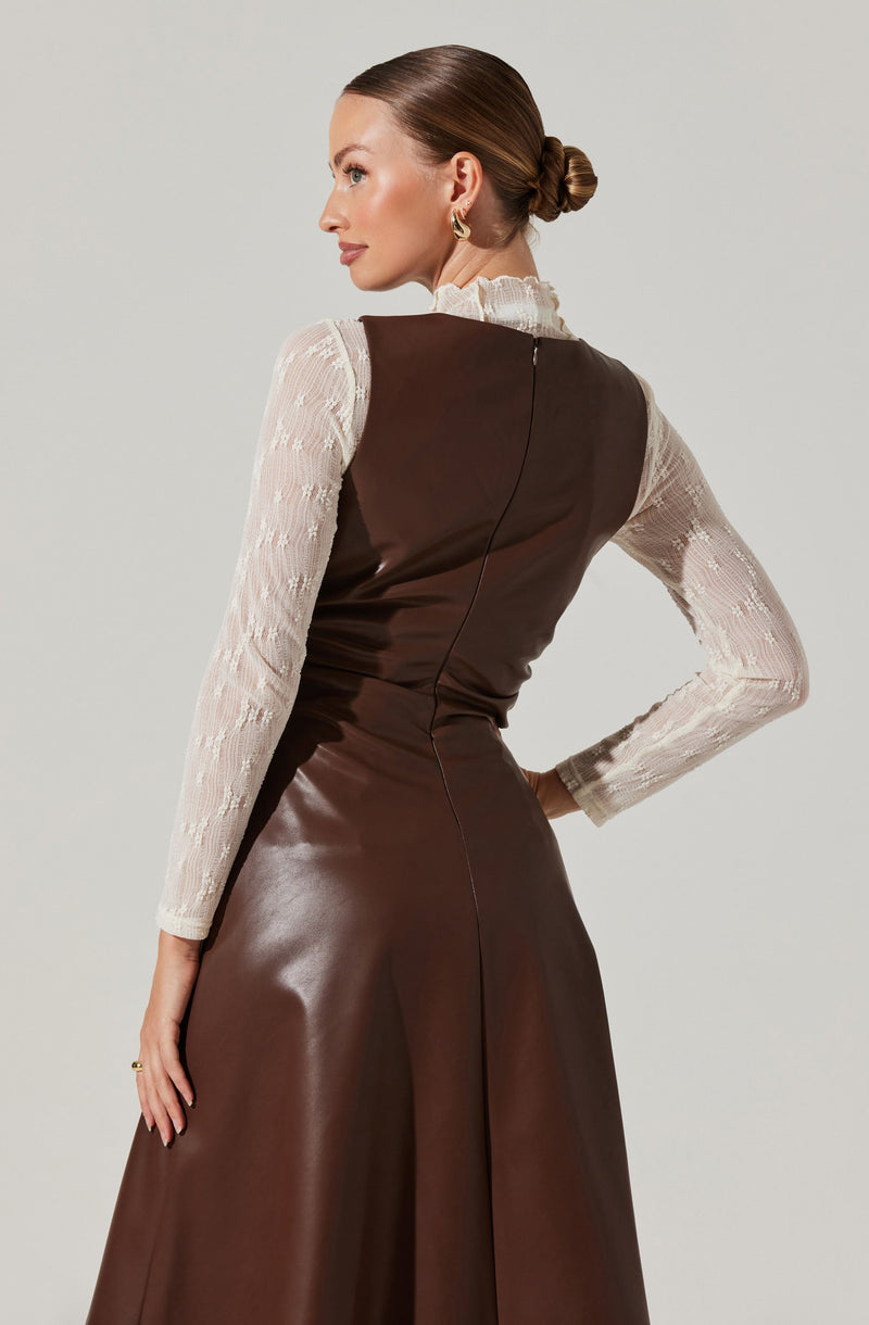 A woman is wearing a long, high-neck, cream-colored lace top with a ruffled collar and long sleeves. Over the top, she has on a sleeveless, fitted, dark brown leather dress that extends to the floor. The back of the dress features a vertical seam running down the center.
