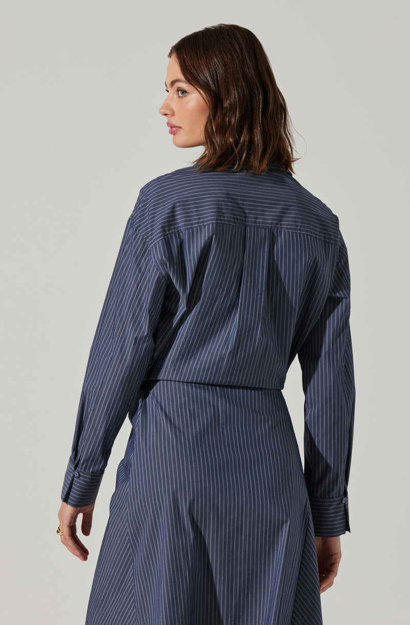 A woman is wearing a long-sleeved, dark navy blue blouse and matching high-waisted pants, both featuring thin, vertical pinstripes in lighter blue. The blouse has a loose fit with a yoke and pleats on the back, and the pants have a tailored fit.