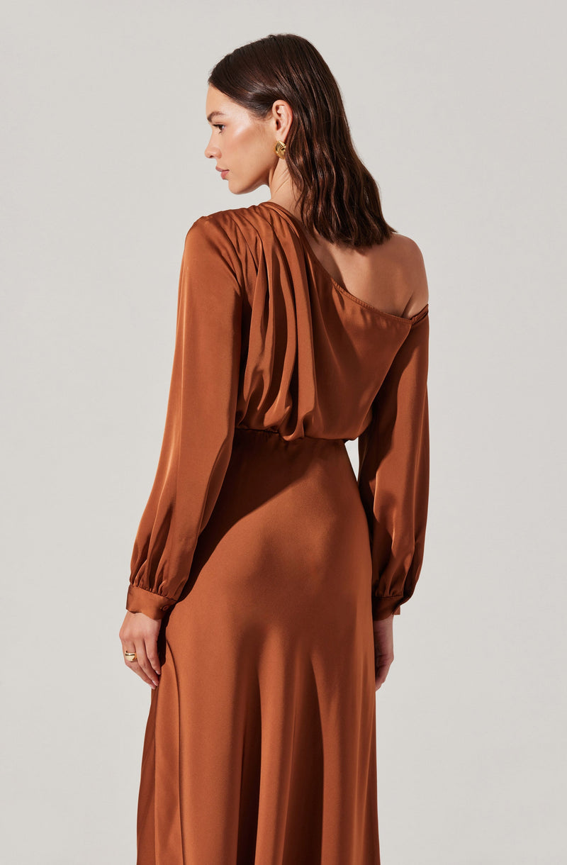 A woman is wearing a long, elegant dress made of shiny, satin-like fabric in a warm, copper-brown color. The dress features long puffed sleeves with fitted cuffs, and the neckline is off-the-shoulder on one side, creating an asymmetrical look.