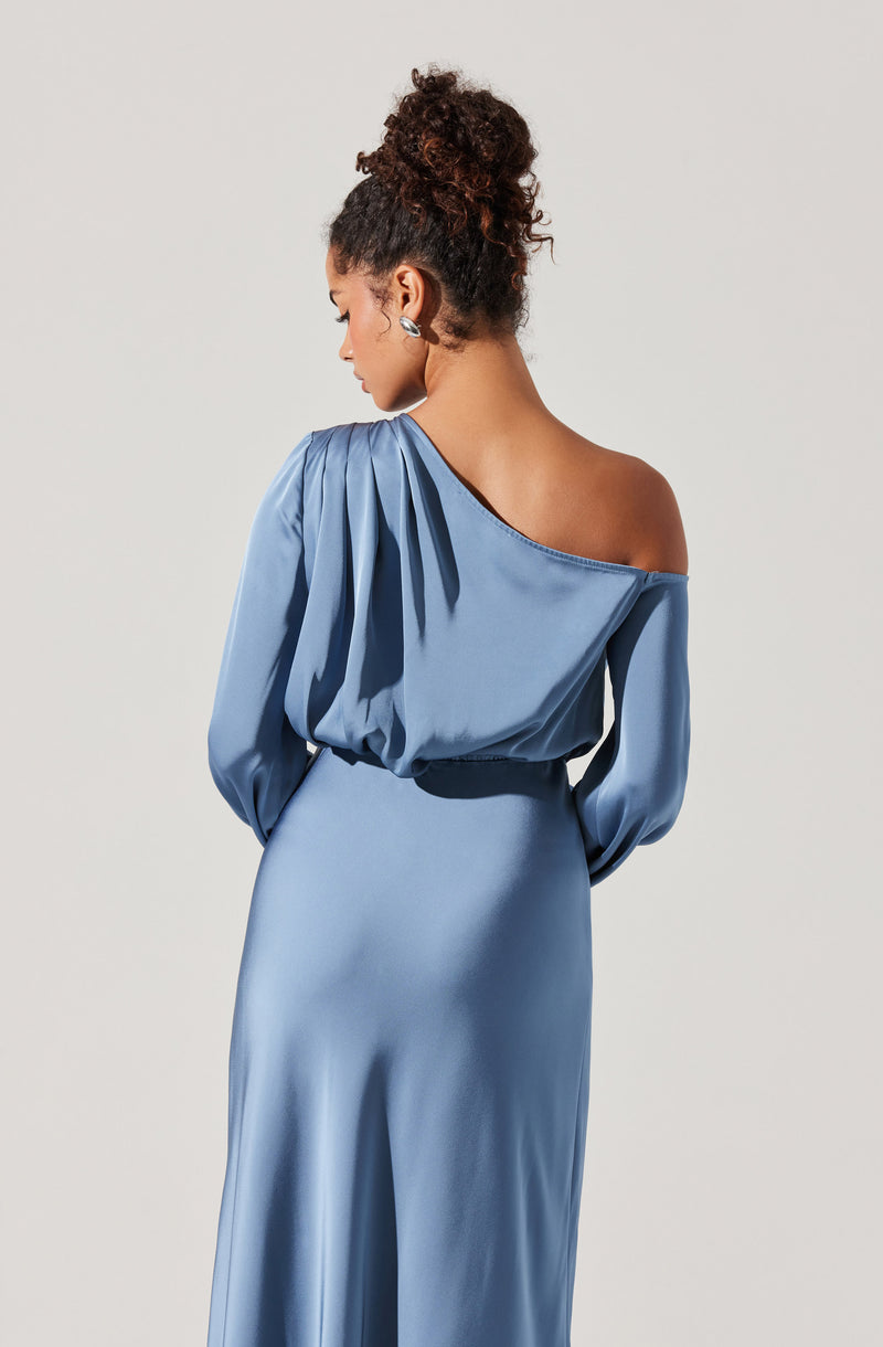 A woman is wearing a shiny, satin-like, blue evening dress with a one-shoulder design. The dress features long, voluminous sleeves gathered at the shoulders, and the waist is cinched with a matching fabric belt. The skirt flows smoothly down to the floor.