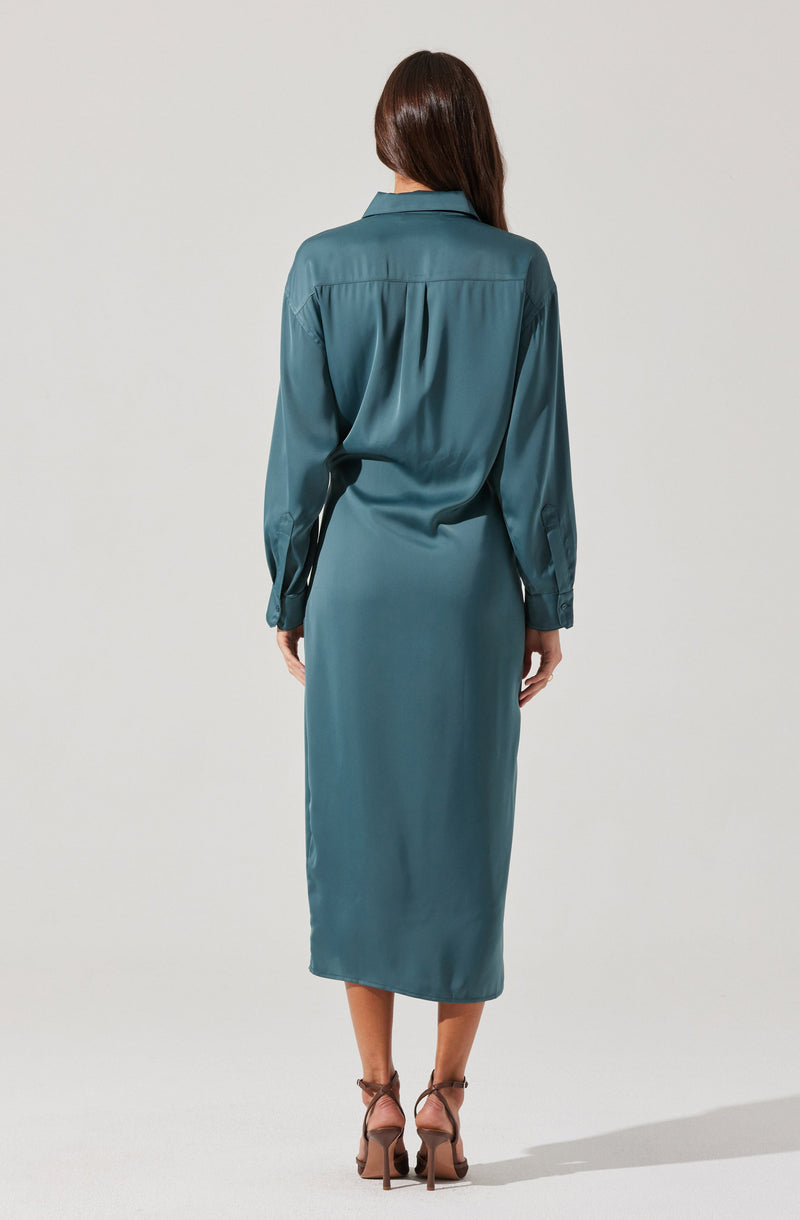 A woman is wearing a long, teal satin dress with long sleeves and a collar. The dress has a buttoned cuffs and a horizontal seam across the back. She is also wearing high-heeled shoes with ankle straps.