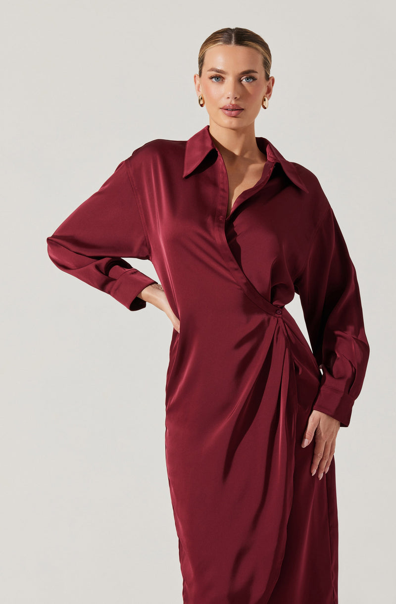 A woman is wearing a long, deep burgundy satin dress with a shiny finish. The dress features a classic collar, button-up front, and long sleeves with cuffs. The waist is cinched with draped fabric, creating a gathered effect that falls into a subtle pleat at the front.