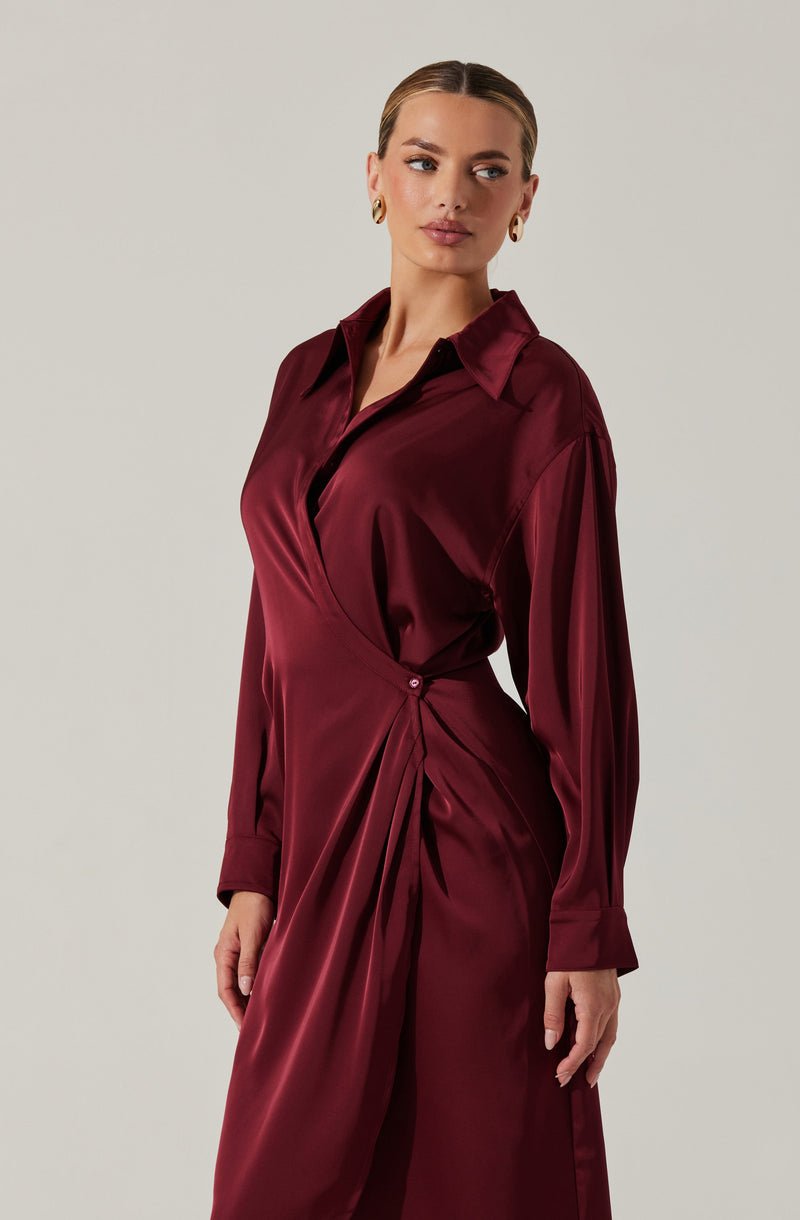 A woman is wearing a deep burgundy satin dress with a collar, long sleeves, and pleated details at the waist. The fabric appears smooth and shiny, giving it an elegant look.