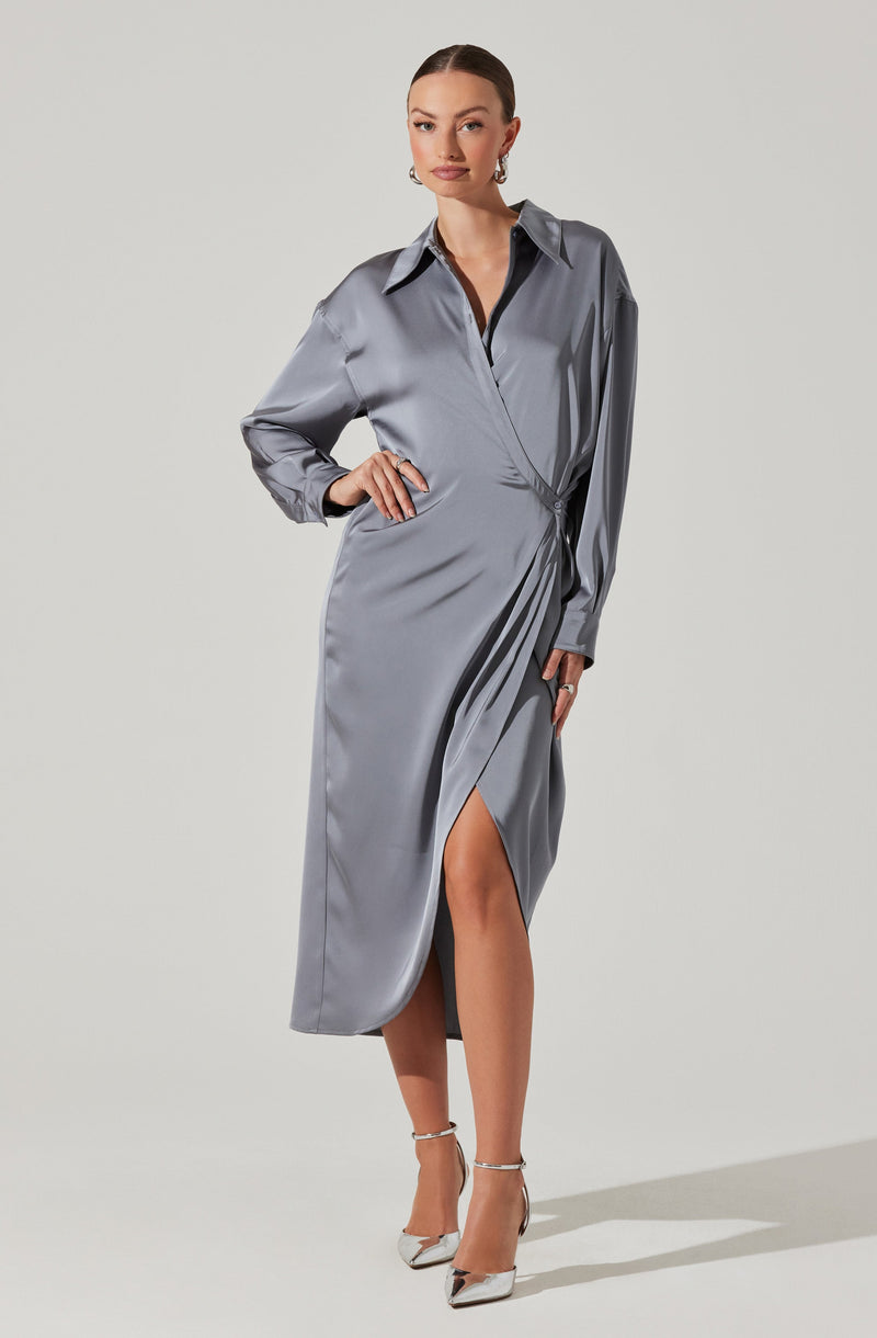 A woman is wearing a long, silver satin dress with a collared neckline and a button-down front. The dress has long sleeves that are slightly puffed at the shoulders and a high slit up one side, revealing her leg. She is also wearing high-heeled shoes with ankle straps.
