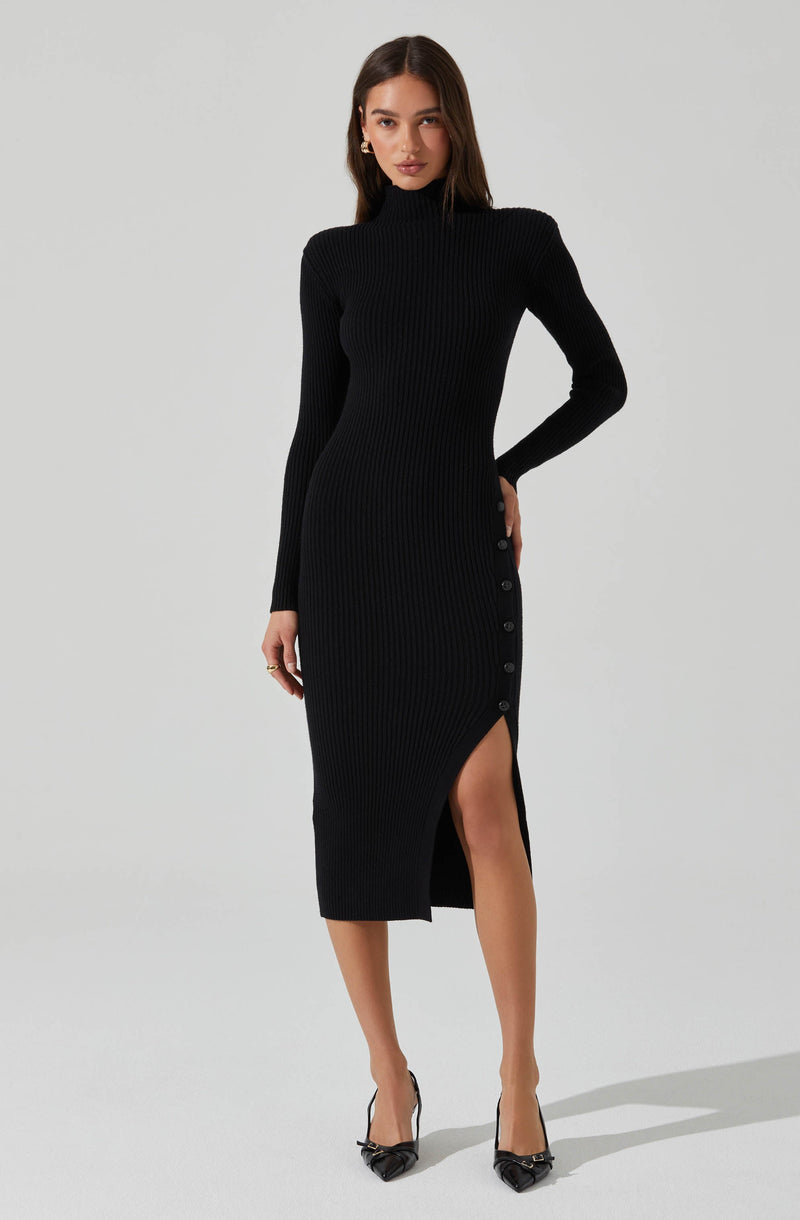 A woman is wearing a fitted, long-sleeve, black ribbed knit dress that extends to mid-calf length. The dress features a high neckline and a row of buttons running along the side from the waist to the hem, with a thigh-high slit revealing part of her leg. She is also wearing black high-heeled shoes with pointed toes and ankle straps.