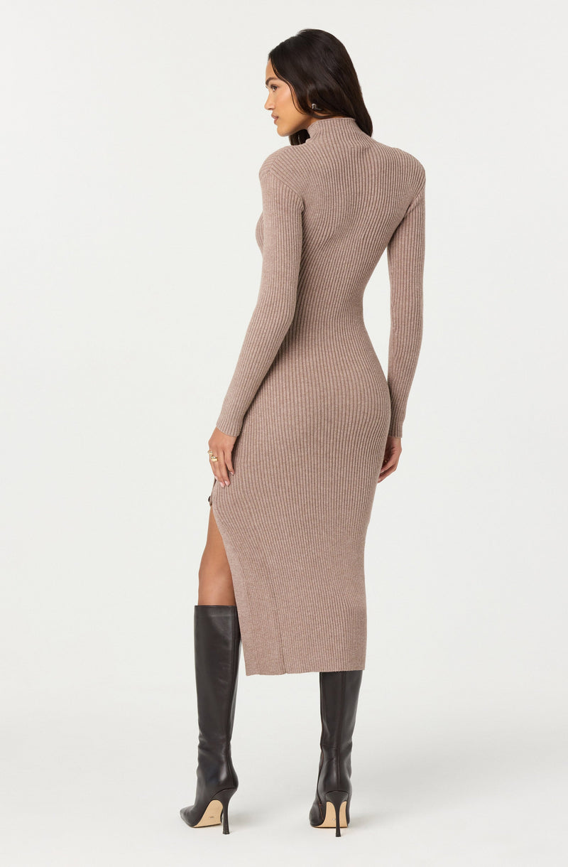 A woman is wearing a long, fitted, ribbed knit dress in a neutral beige color that extends to mid-calf and features a slit on one side. She has on tall black leather high-heeled boots that reach just below her knees.