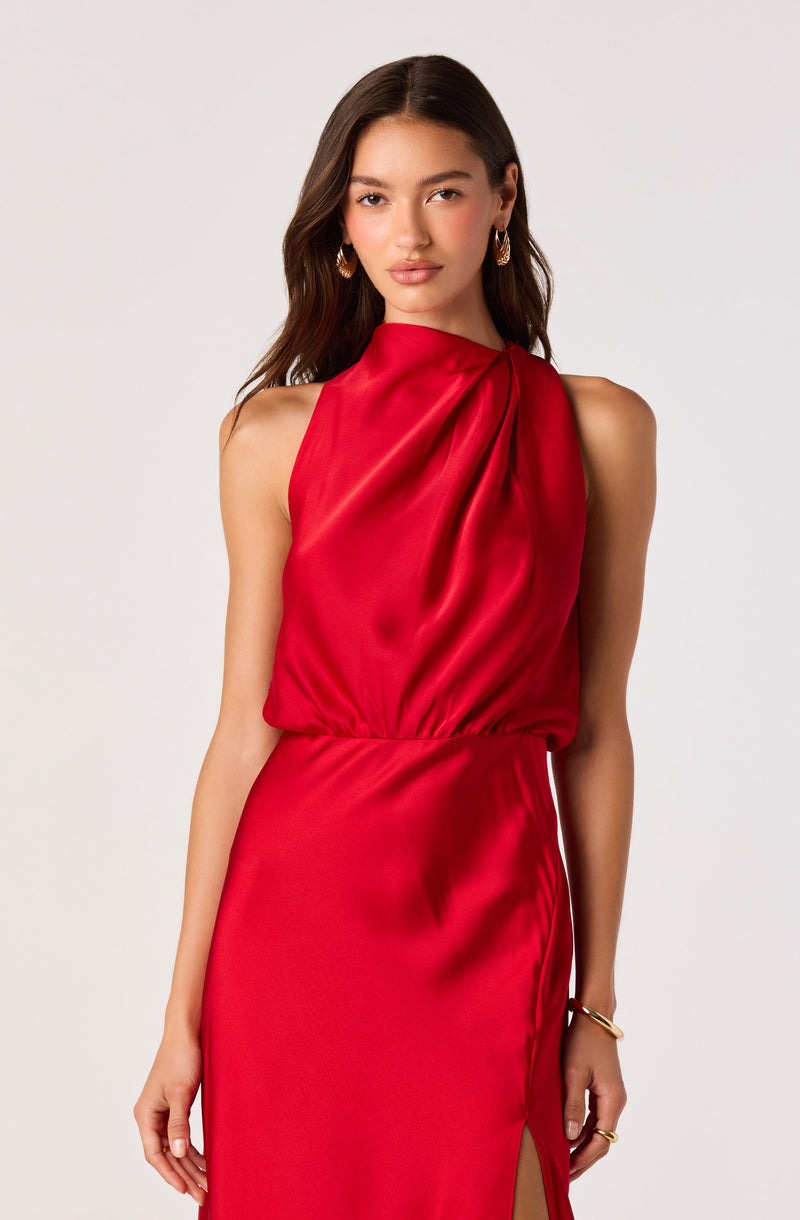 Woman in a sleeveless, satin red dress with draped details and a slit on the side.