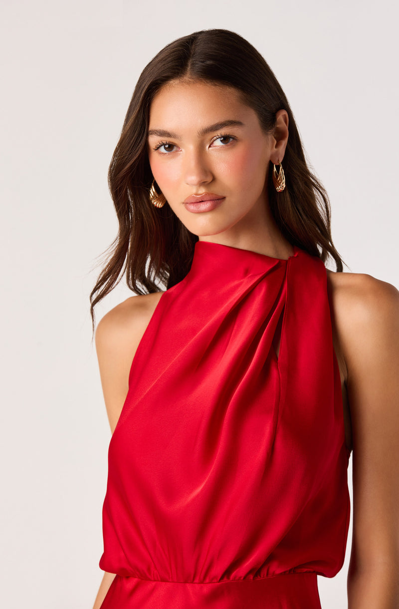 Woman wearing a sleeveless, red satin dress with pleats on the shoulder.