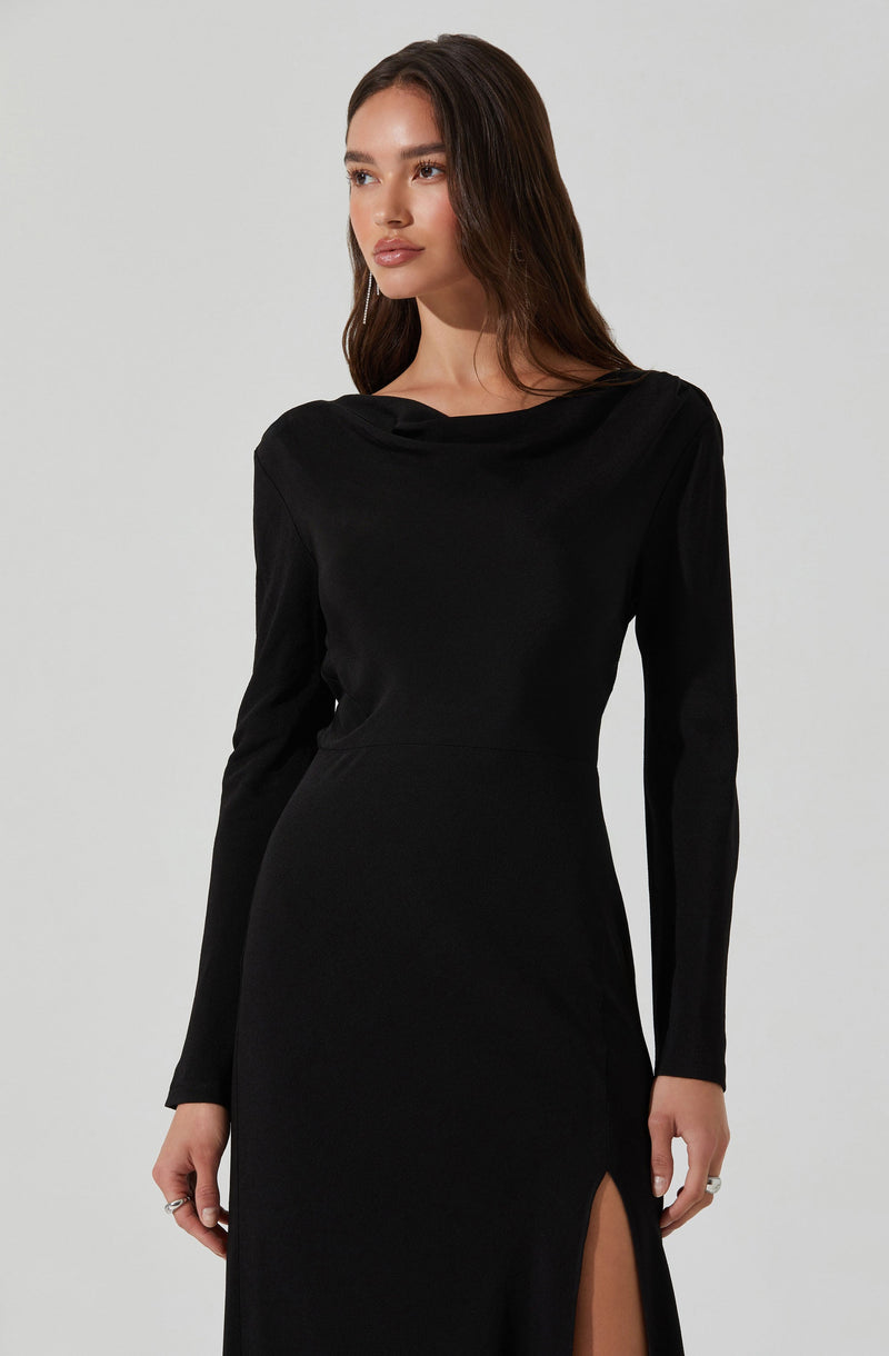 A woman is wearing a long black dress with a boat neckline and long sleeves. The dress has a slit on the side, revealing part of her leg.