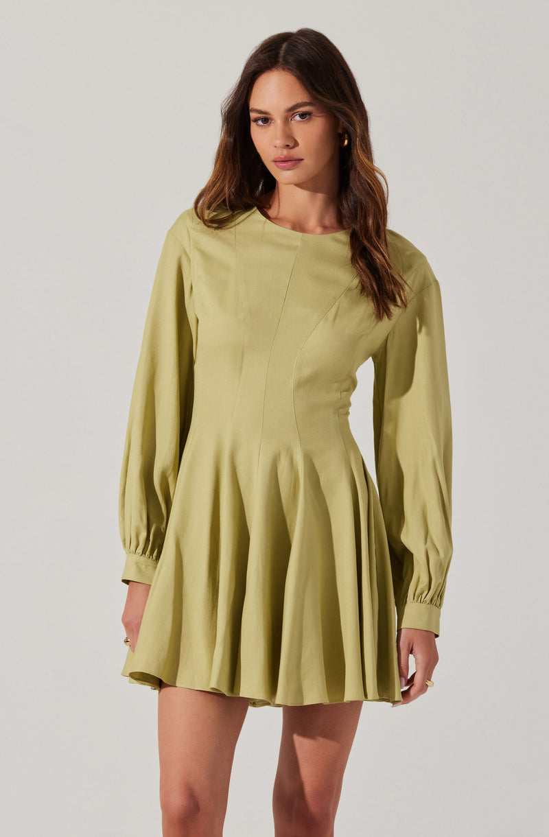 A woman is wearing a light green dress with long, puffed sleeves that are gathered at the wrists with cuffs. The dress has a fitted bodice with vertical seam details and a flared, pleated skirt that falls above the knees. The fabric appears to be smooth and slightly shiny.
