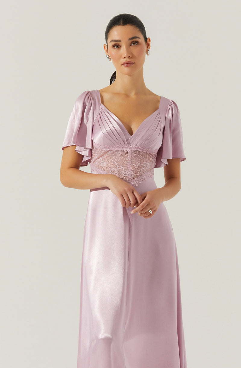 A woman is wearing a light pink, shiny satin dress with short, puffed sleeves that have ruffled details. The dress has a V-neckline and a fitted bodice with lace detailing at the waist, creating a delicate and elegant look.