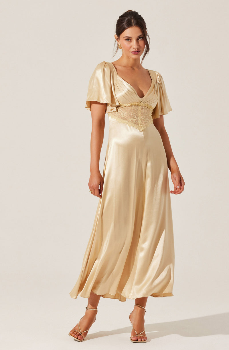 A woman is wearing an elegant, floor-length cream-colored satin gown with short, puffy sleeves. The dress features a fitted bodice with a deep neckline and lace detailing around the waist. She is also wearing strappy high-heeled sandals.