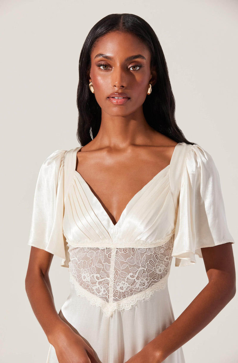 A woman is wearing an elegant cream-colored dress with a deep V neckline. The dress features puffed short sleeves made of shiny satin fabric and a fitted bodice with a lace panel at the waist, adding a touch of delicate detail. The dress has a gathered, flowing skirt.