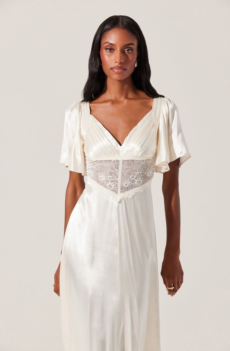A woman is wearing a cream-colored satin dress with short, puffed sleeves. The dress features a V-neckline, a lace panel at the waist, and pleated detailing on the bodice. The fabric appears smooth and shiny, draping elegantly down to the floor.