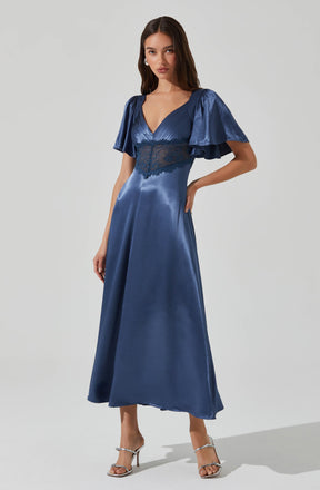 A woman is wearing a floor-length, shiny blue satin dress with a deep V neckline. The dress features short, puffy sleeves made of the same shiny blue satin fabric. There is a lace panel beneath the bust area that extends around the waist, adding a delicate detail to the dress. She is also wearing silver high-heeled sandals with thin straps.