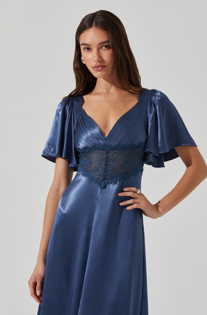A woman is wearing a deep blue satin dress with a V-neckline. The dress features short, puffed sleeves with a ruffled, shiny satin finish. The bodice has pleated detailing and a wide lace band at the waist, adding texture and contrast. The skirt is smooth, flowing, and made of satin fabric.