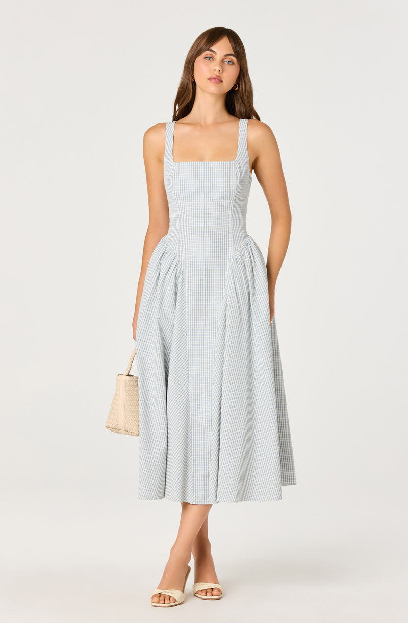 Woman in a blue and white checkered sleeveless sundress with wide straps, gathered skirt, and square neckline.