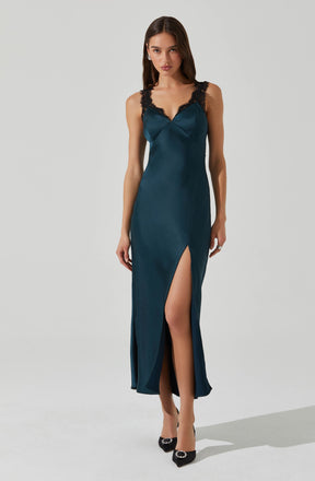 A woman is wearing a long, teal satin evening gown with black lace shoulder straps. The dress features a sweetheart neckline, a high slit on the front left side revealing her leg, and a fitted silhouette that reaches the floor. She is also wearing black high heels with embellishments and pearl earrings.