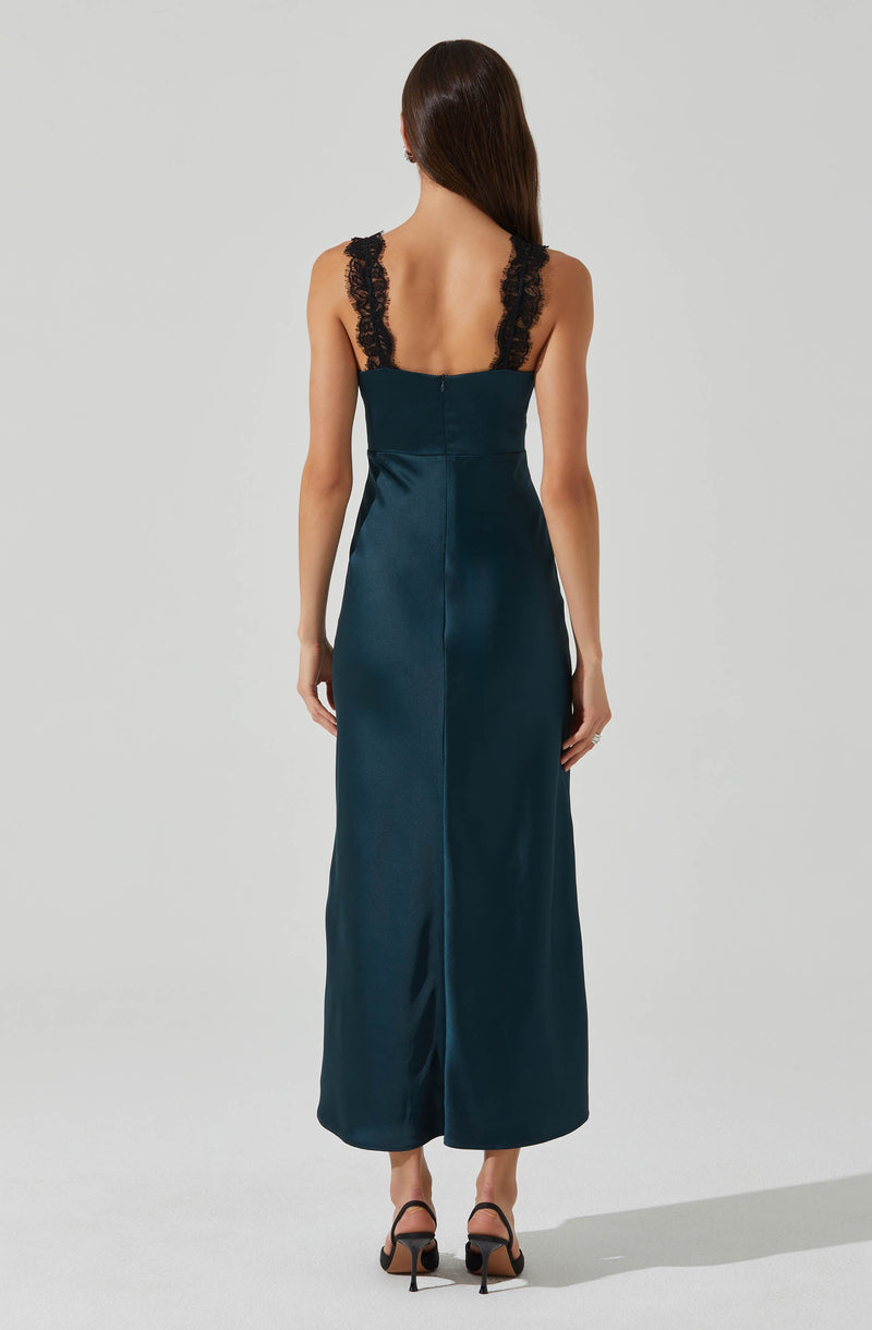 A woman is wearing a long, sleeveless, teal satin gown with a fitted bodice and a back zipper. The dress features black lace straps that extend over her shoulders. She is also wearing black high-heeled sandals.