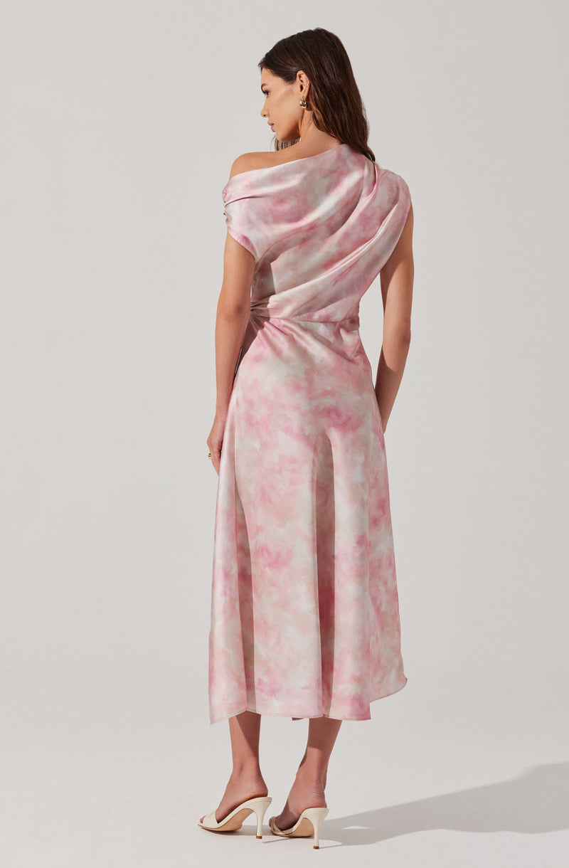 A woman is wearing a pink and white tie-dye dress with an off-shoulder design on one side, featuring a draped bodice and a fitted waist. The dress transitions into flowing wide-leg pants that reach mid-calf. She is also wearing white high-heeled shoes.