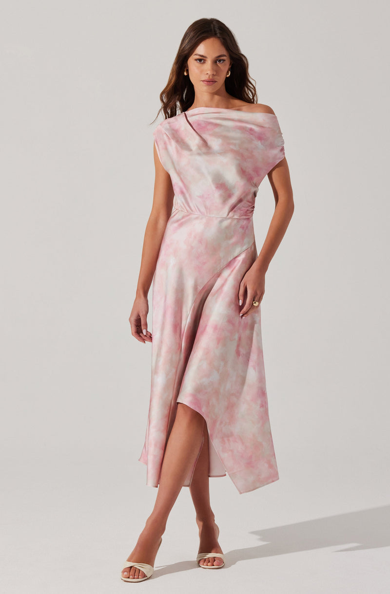 A woman is wearing a sleeveless, off-the-shoulder dress with a pink and white tie-dye pattern. The dress has a fitted waist and a flowing, asymmetrical hemline that is longer in the back and higher in the front, revealing her legs. She is also wearing open-toe heels and gold hoop earrings.