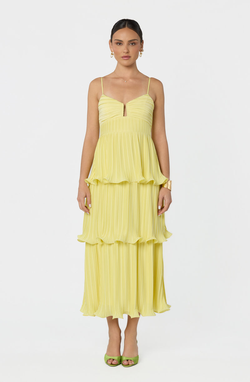 Woman in a yellow layered pleated dress with thin straps, paired with green open-toe heels.