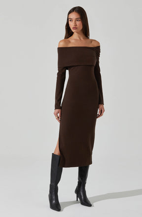 A woman is wearing a long, dark brown off-shoulder dress with long sleeves. The dress is fitted and reaches down to her ankles, with a slit on one side. She is also wearing black knee-high heeled boots.