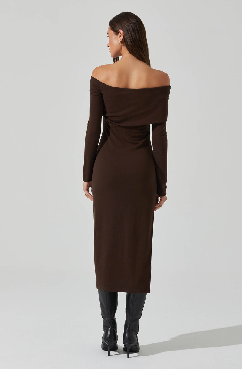 A woman is wearing a long, dark brown, off-the-shoulder dress that extends down to her ankles. The dress features long sleeves and a fitted silhouette. She has paired the dress with black knee-high boots with high heels.