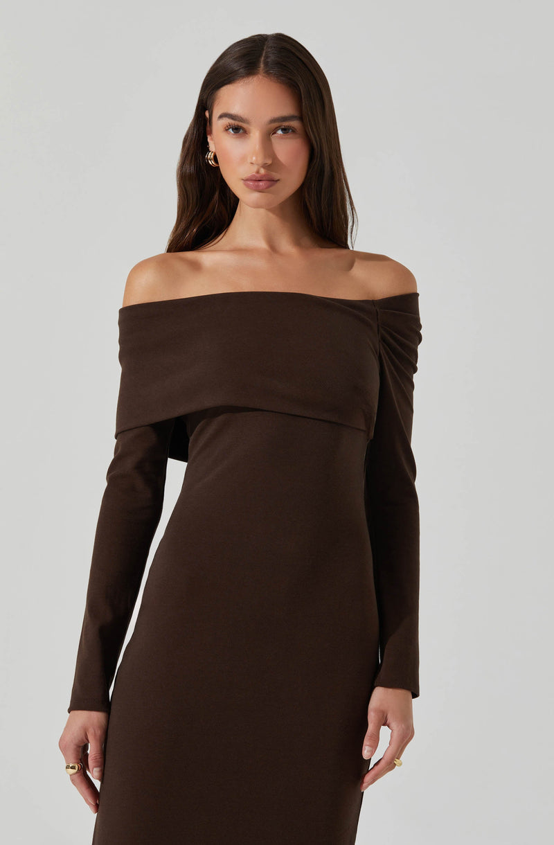 A woman wearing an off-the-shoulder, long-sleeved dress in a rich, dark brown color. The dress features a layered, wide neckline that drapes over her shoulders and upper arms, creating a sophisticated and stylish look. The fabric appears smooth and slightly stretchy, fitting her figure closely.