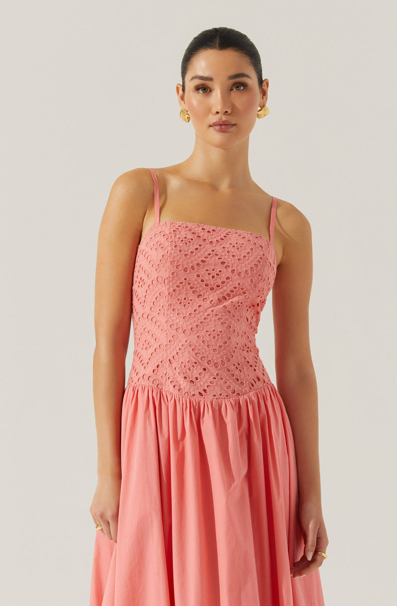 A woman is wearing a sleeveless, peach-colored dress with thin spaghetti straps. The upper part of the dress features a textured, eyelet lace pattern, while the lower part is made of a gathered, solid fabric that flows down in a full skirt.
