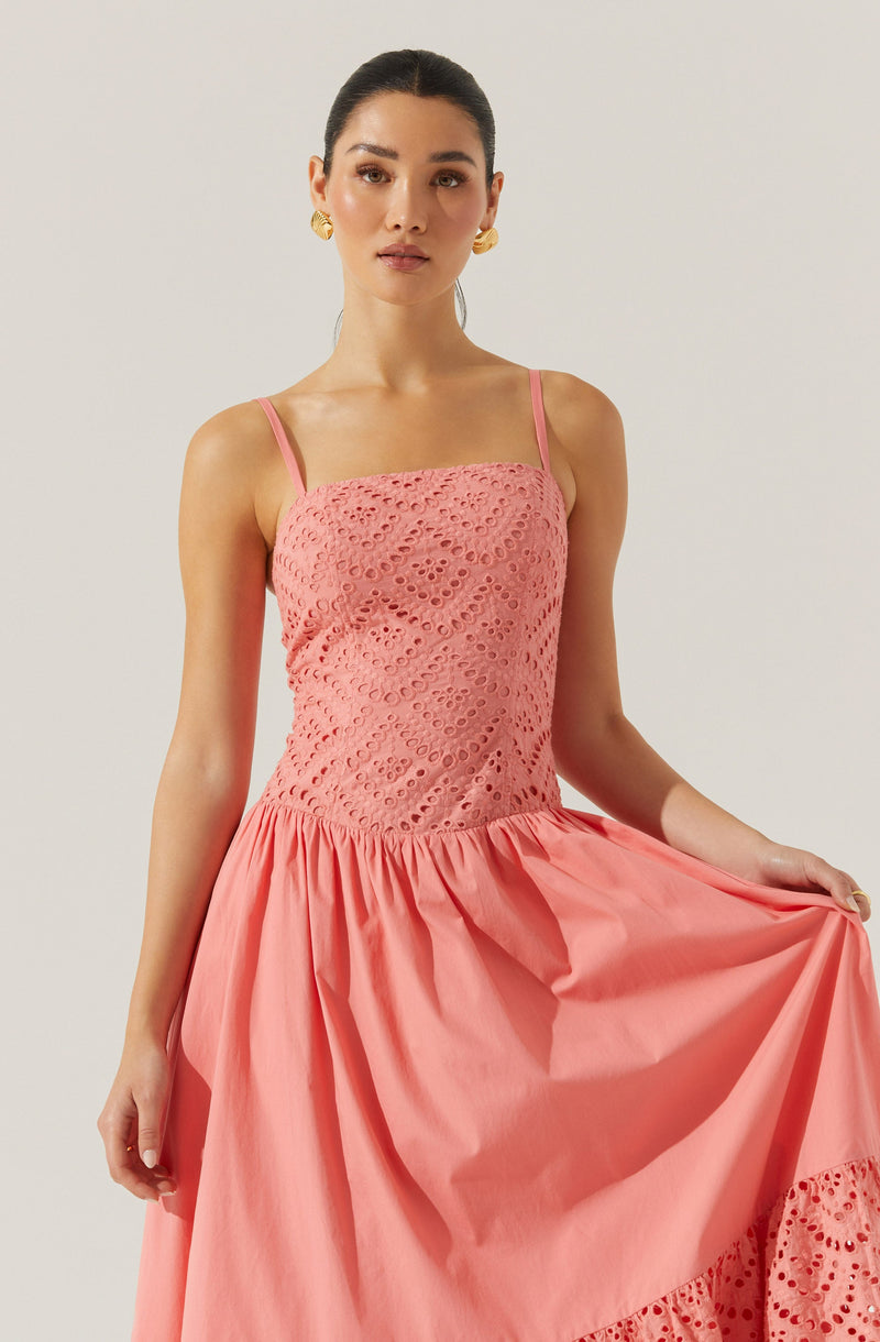 The dress features a sleeveless design with thin shoulder straps. The bodice is made of pink lace fabric with a circular cut-out pattern. The skirt is made of solid pink fabric, gathered at the waist, and has decorative lace detailing near the hem.