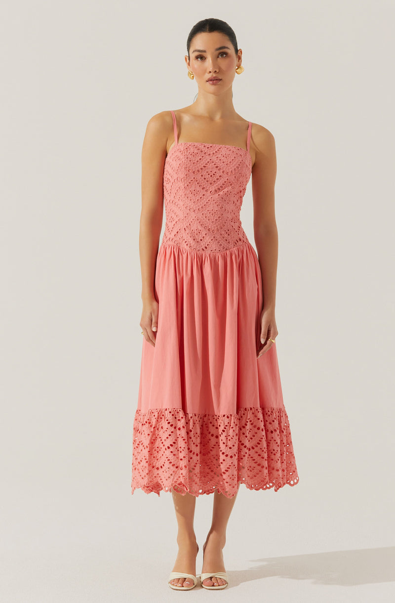 The dress is a sleeveless, pink midi with thin spaghetti straps. The upper part features intricate eyelet lace patterns, and the skirt is gathered with a wide band of matching eyelet lace at the hem, creating a scalloped edge.