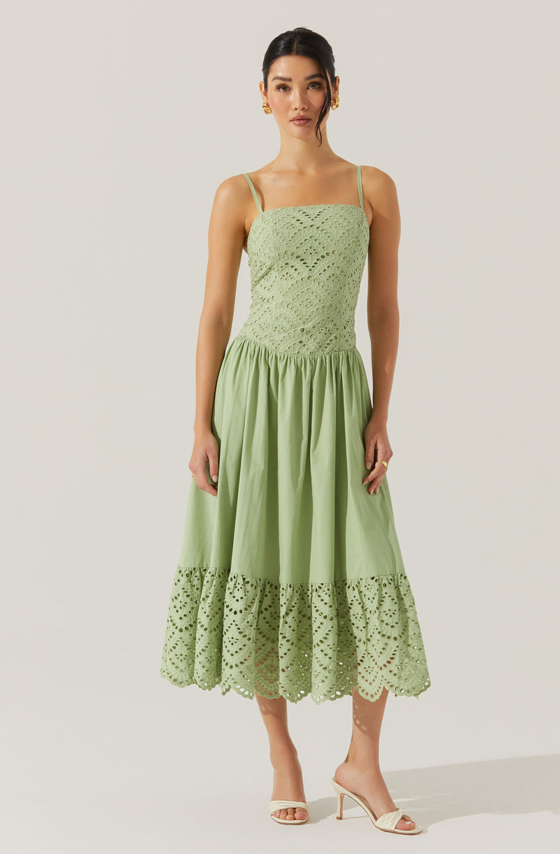 A woman is wearing a light green dress with a fitted, crocheted, sleeveless bodice featuring a pattern of openwork stitches. The dress has spaghetti straps and a full, gathered skirt with a band of eyelet embroidery at the hem.