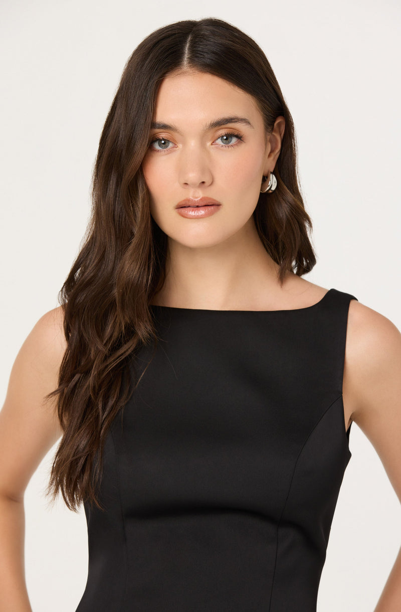 A woman is wearing a sleeveless black dress with a boat neckline.