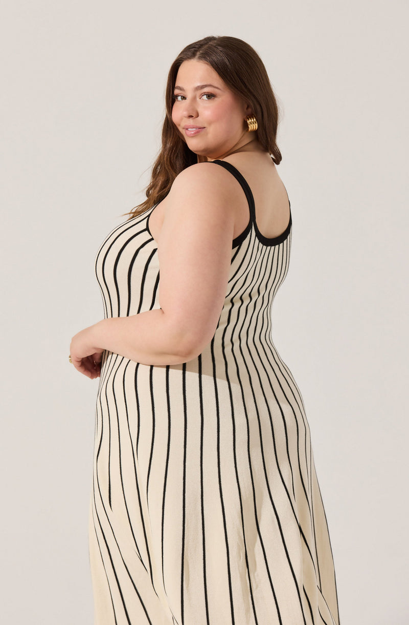 A woman is wearing a sleeveless dress with thin black straps and a fitted bodice. The dress features vertical black stripes on a beige background, creating a classic pinstripe pattern throughout.