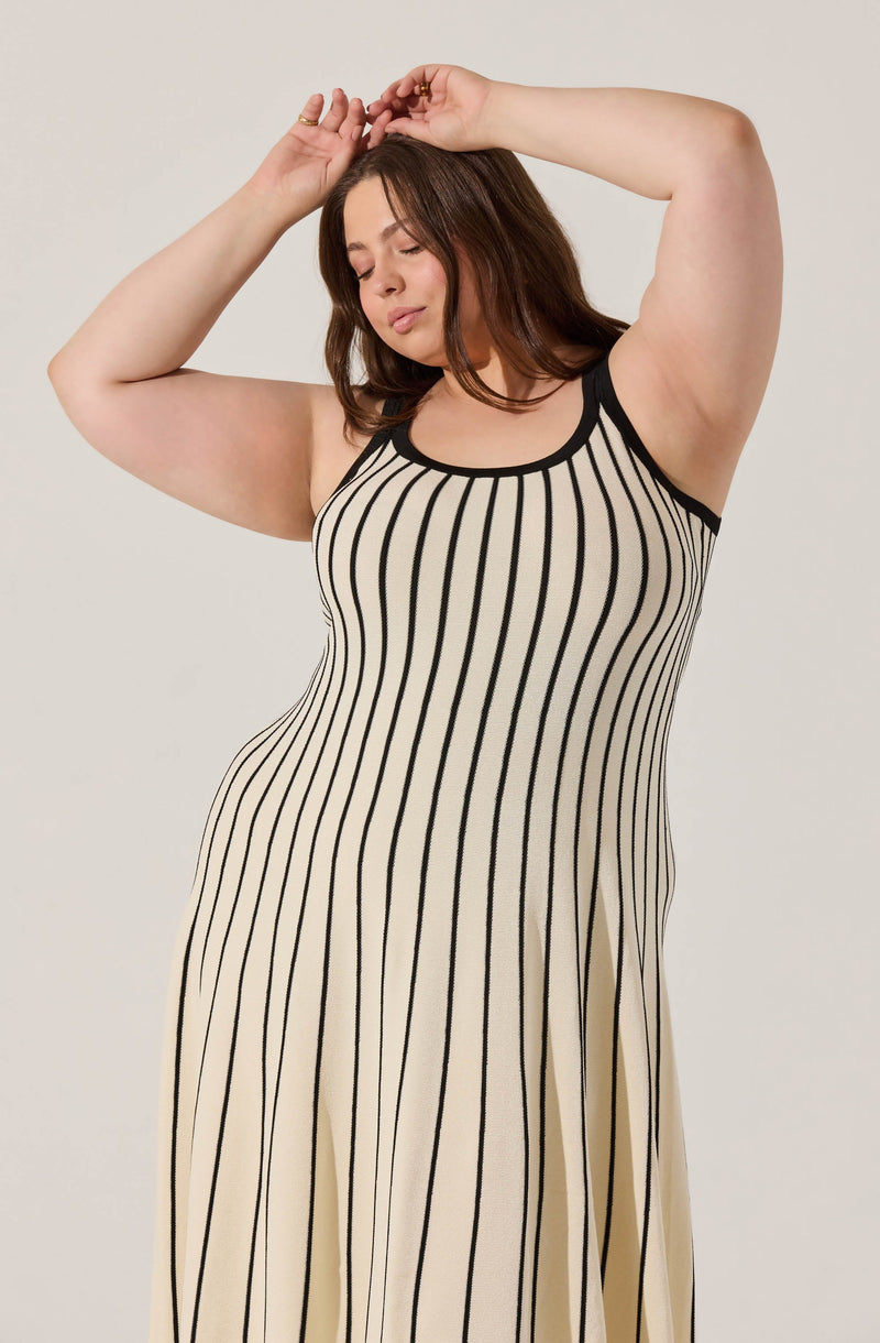 A woman is wearing a sleeveless, ankle-length dress with vertical black and cream stripes. The dress has a black trim around the rounded neckline and armholes.
