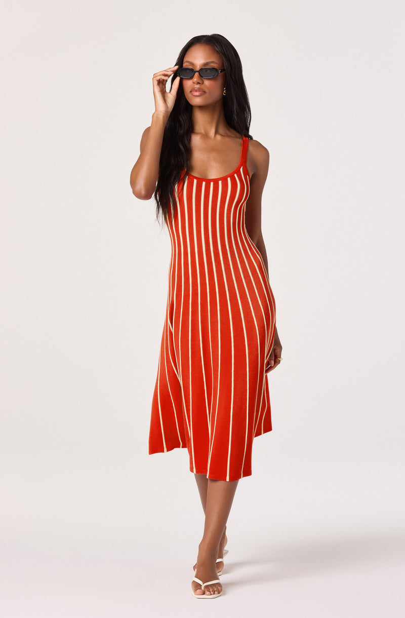 A woman wearing a red midi dress with white vertical stripes, paired with black sunglasses.