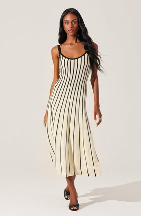A woman is wearing a sleeveless, ankle-length dress with vertical black and beige stripes. The dress has black shoulder straps and black trim around the neckline and armholes. She is also wearing black high-heeled sandals.