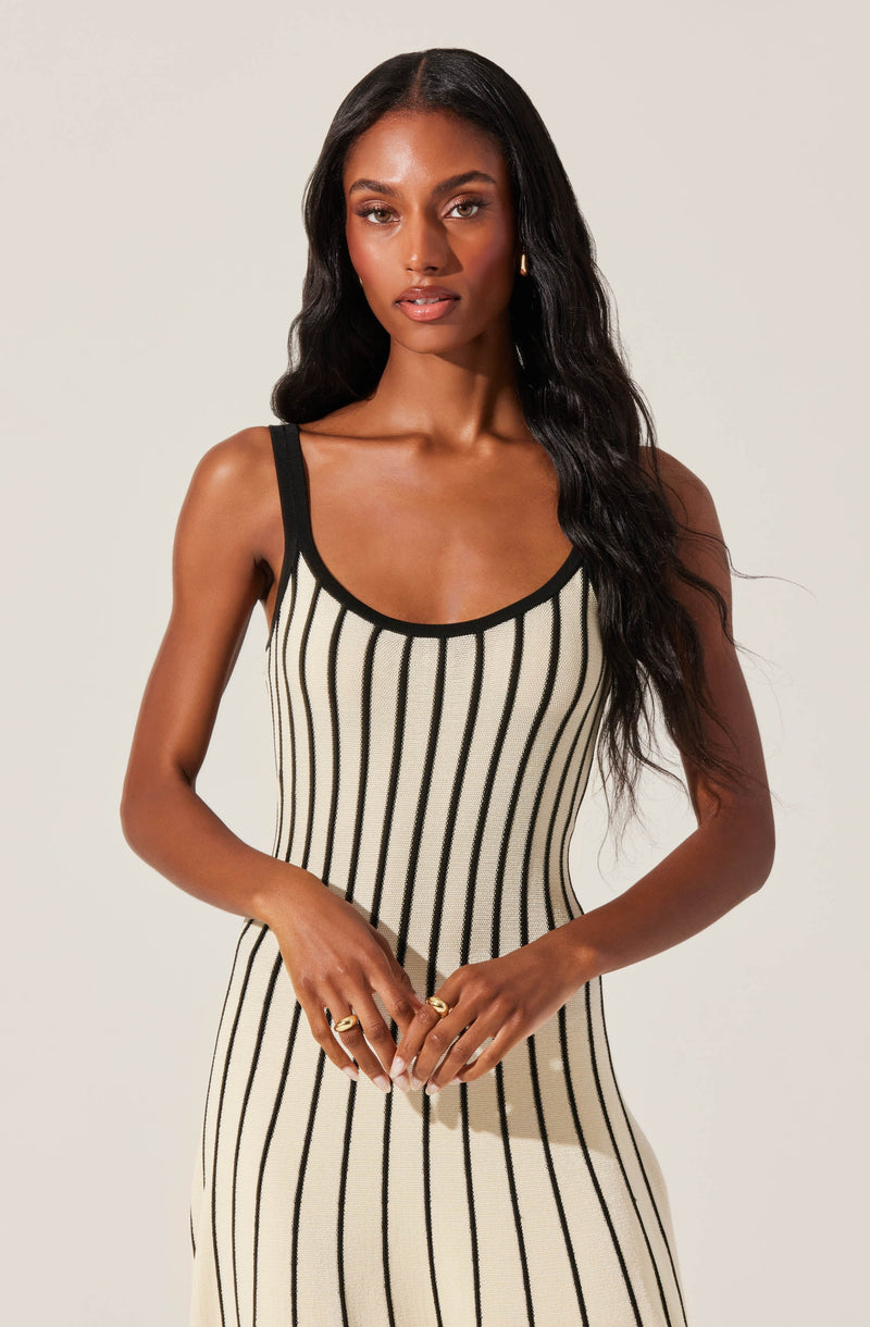 A woman is wearing a sleeveless, fitted dress with black vertical stripes on a cream-colored background. The dress has black straps and black trim around the neckline.