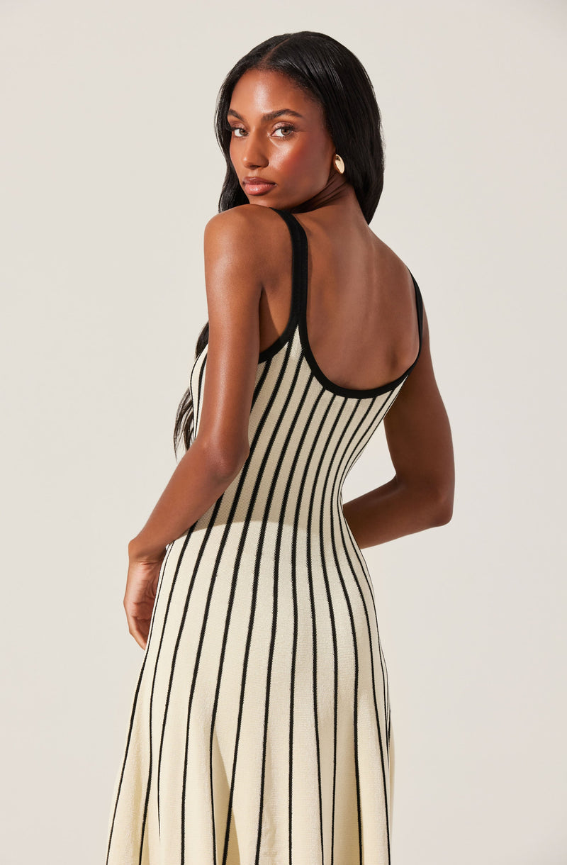 A woman is wearing a sleeveless, fitted dress with vertical black stripes on a cream-colored background. The dress features black trim along the armholes and neckline.
