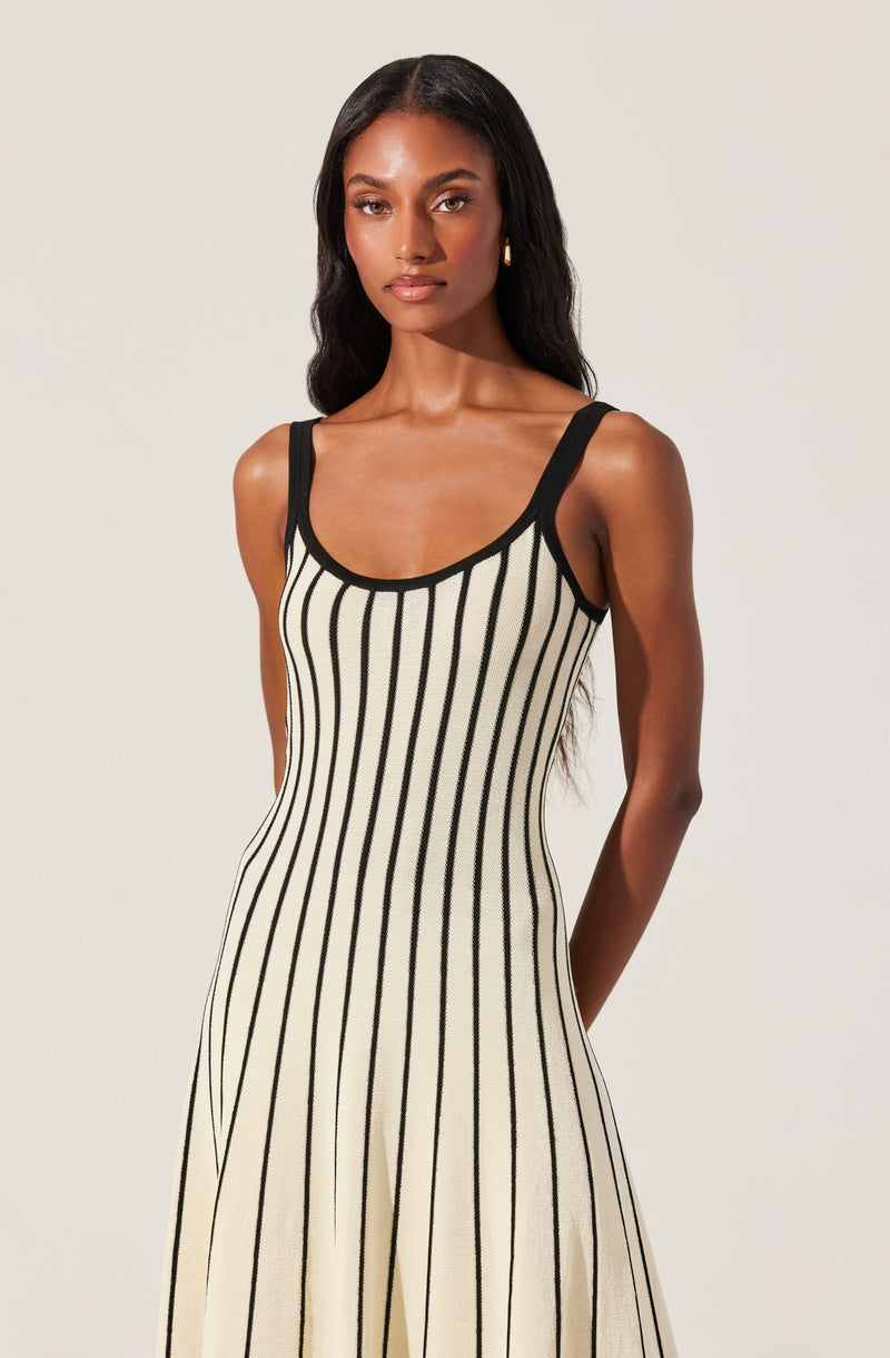 A woman is wearing a sleeveless, beige dress with vertical black stripes. The dress features black straps and black trim around the neckline.