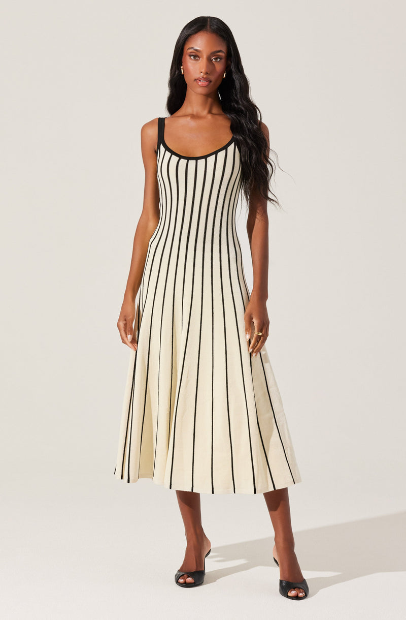 A woman is wearing a sleeveless, ankle-length dress with vertical black stripes on a cream-colored fabric. The dress features black trim around the neckline and straps.