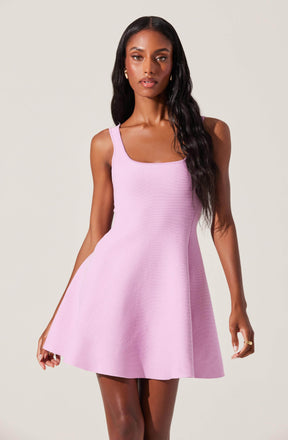 A woman is wearing a sleeveless, light purple dress with a fitted bodice and a flared skirt that falls above the knees. The dress has wide shoulder straps and a square neckline.