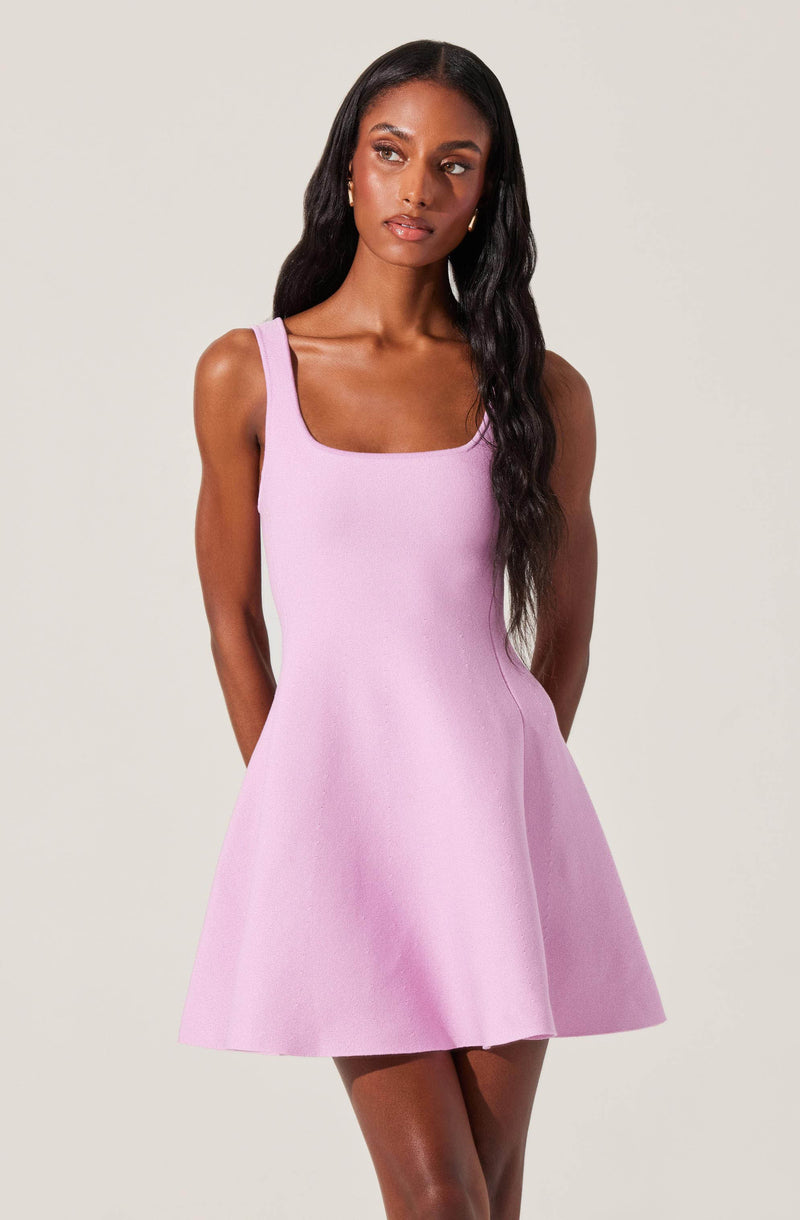 A woman is wearing a sleeveless, pastel pink dress with thick straps, a fitted bodice, and a flared skirt that falls above the knees.