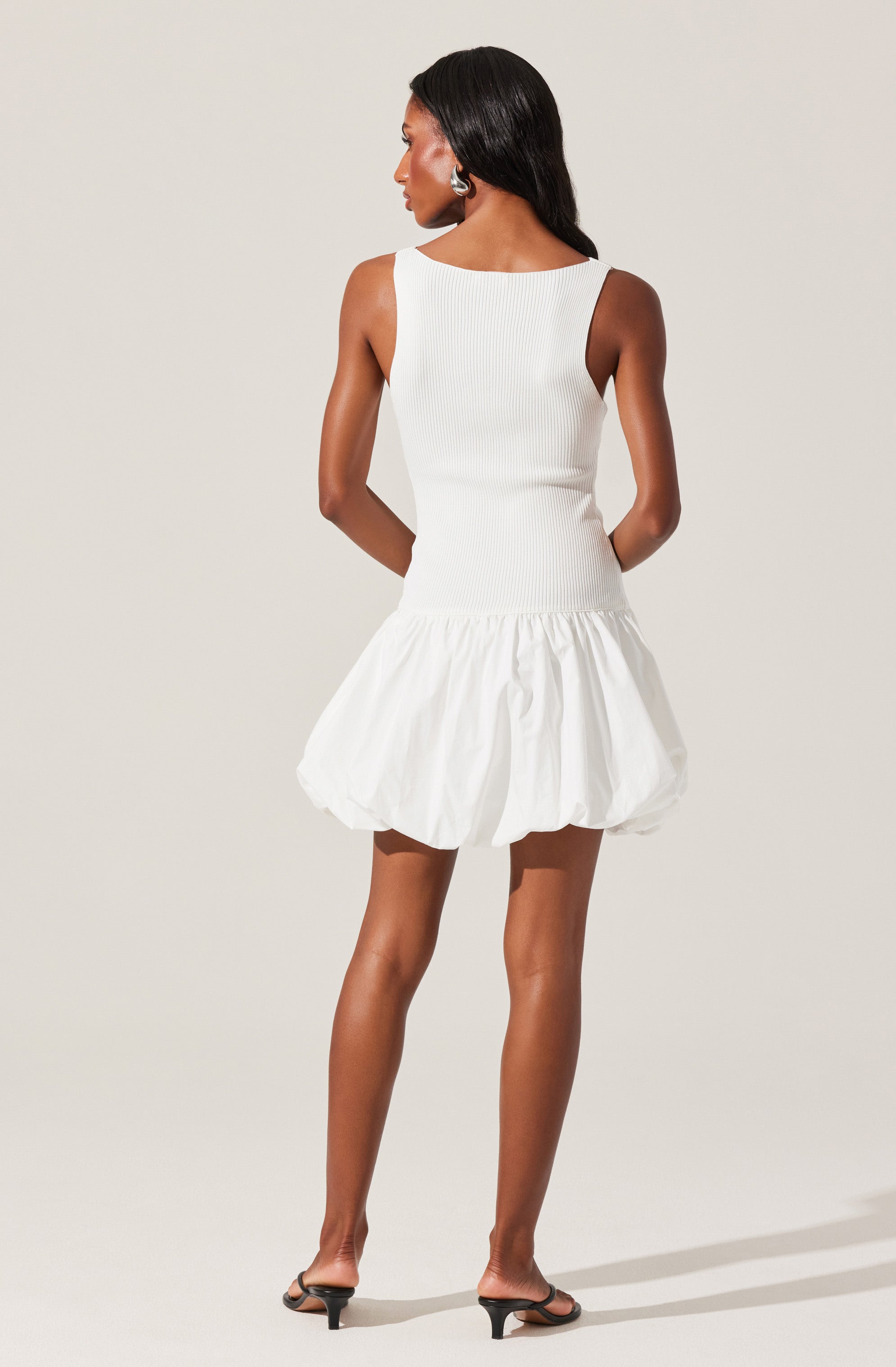 A woman is wearing a sleeveless, fitted white top with a round neckline and a voluminous, bubble-style white skirt that has a gathered, puffy appearance.