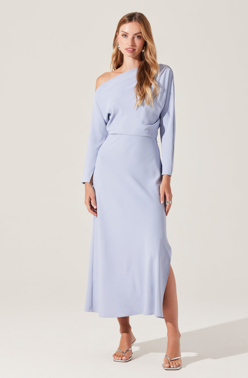 A woman is wearing a long, light blue dress with an asymmetrical neckline that drapes over one shoulder. The dress has long sleeves and a slit up one side, revealing her leg. She is also wearing high-heeled sandals with thin straps.