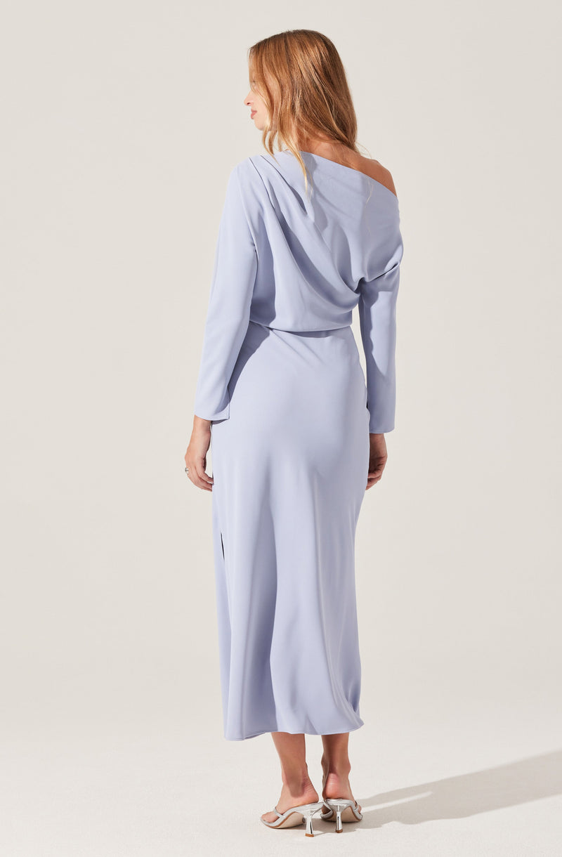 A woman is wearing a light blue, long-sleeved, off-the-shoulder dress with a loose, draped top and a fitted waist. The dress has a silky, flowing fabric and reaches down to her ankles. She is wearing beige high-heeled sandals.